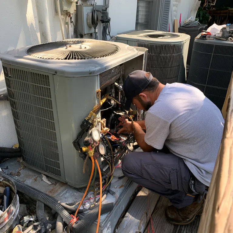 Technician working on the wiring of an outdoor air-conditioning condenser with gauges connected