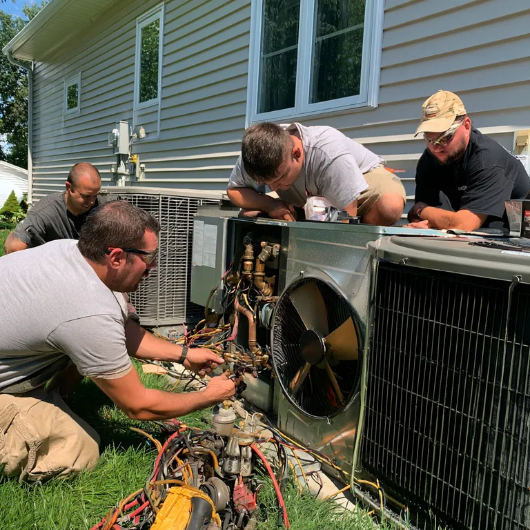 Several technicians working together on outdoor HVAC equipment beside a home